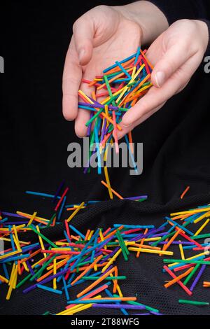 Main laissant des bâtons en bois de couleur tomber sur fond noir Banque D'Images