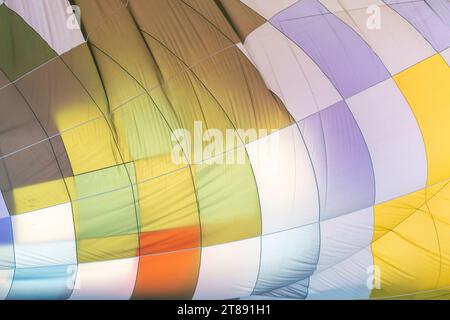 Détail abstrait d'une montgolfière multicolore, partiellement gonflée, prête pour le vol. La lumière du soleil du matin brille à travers le tissu. Banque D'Images