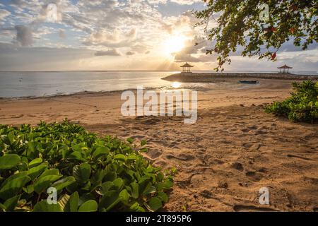 Lever de soleil magique avec des nuages dans le ciel. Ciel spectaculaire sur la plage de Sanur, Denpasar à Bali. Temple dans la mer calme le matin. Paysage tropical photographié Banque D'Images