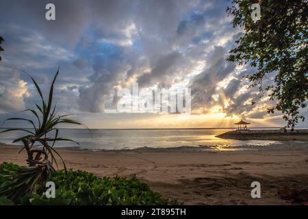 Lever de soleil magique avec des nuages dans le ciel. Ciel spectaculaire sur la plage de Sanur, Denpasar à Bali. Temple dans la mer calme le matin. Paysage tropical photographié Banque D'Images