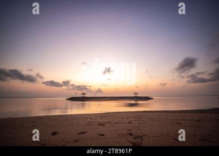 Lever de soleil magique avec des nuages dans le ciel. Ciel spectaculaire sur la plage de Sanur, Denpasar à Bali. Temple dans la mer calme le matin. Paysage tropical photographié Banque D'Images