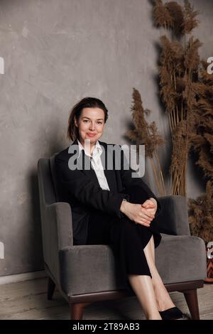 une femme en costume d'affaires est assise dans une chaise dans le bureau Banque D'Images