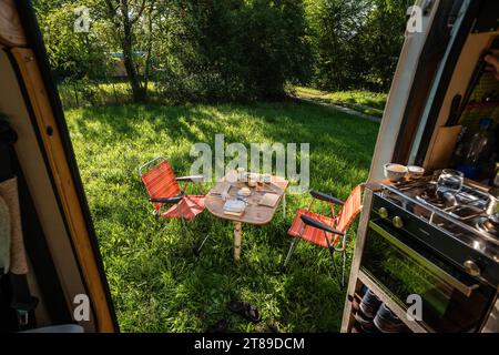 Ein Camper steht zwischen Bäumen an einem sonnigen Sommertag auf einer Wiese im Grünen, ein gedeckter Frühstückstisch mit Stühlen steht vor der Schiebetür des campeurs. Regensburg, Bayern, Deutschland. In der Altstadt von Regensburg *** Un camping-car se tient entre les arbres lors d'une journée ensoleillée d'été sur une prairie dans la campagne, une table de petit-déjeuner posée avec des chaises se tient devant la porte coulissante du camping-car Regensburg, Bavière, Allemagne dans la vieille ville de Regensburg crédit: Imago/Alamy Live News Banque D'Images