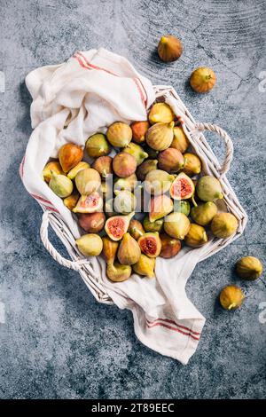 Figues vertes biologiques fraîchement cueillies dans un panier sur fond gris Banque D'Images