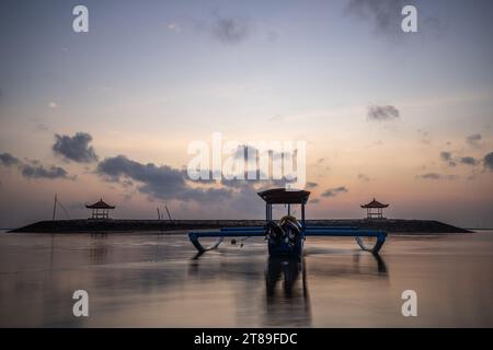 Lever de soleil sur la plage de sable de Sanur. Temple dans l'eau. Bateau de pêche traditionnel, Jukung sur la plage. Foi hindoue à Sanur sur Bali. Île de rêve Banque D'Images