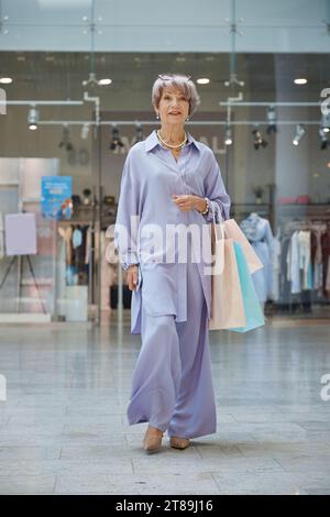 Portrait en longueur de femme âgée avec des sacs à provisions au-dessus de la vitrine du magasin Banque D'Images