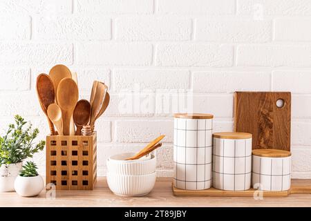 Ensemble de pots de conservation des aliments en céramique élégants, bols en céramique, cuillères en bois dans un stand sur un comptoir en bois avec des plantes d'intérieur en pot Banque D'Images