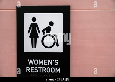 Gros plan du signe de salle de bain des femmes contre le mur de couleur rose avec des symboles pour femme et fauteuil roulant. Espace de copie. Banque D'Images