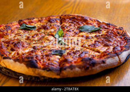 Une image rapprochée d'une pizza fraîchement cuite avec des feuilles de basilic vert éparpillées sur le dessus, assise sur une table en bois Banque D'Images