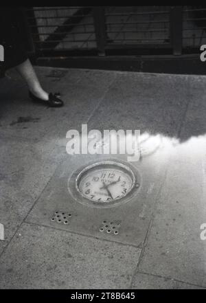 Années 1950, historique, une horloge couchée dans un trottoir, Thames Street, Windsor, Berkshire, Angleterre, ROYAUME-UNI. Sir Cyril Dyson, bijoutier et horloger pour la reine, avait installé l'horloge en mai 1950 dans le trottoir à l'extérieur de sa boutique comme vitrine pour ses talents d'horloger. À l'époque, c'était la seule horloge de chaussée au monde. Banque D'Images