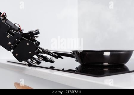 Véritable main de robot et poêle à frire sur cuisinière électrique. Concept d'automatisation de processus robotisée Banque D'Images