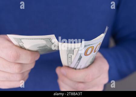 Un homme dans un sauteur bleu tient une pile de 100 dollars dans ses mains close-up et compte them.money concept. Photo de haute qualité Banque D'Images