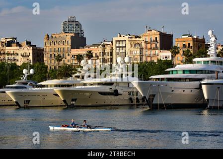 Les Scullers passent devant les super yachts de millionnaires amarrés à Marina Port Vell, pris de la Moll d'Espanya, Barcelone, Catalogne, Espagne, Europe. Banque D'Images