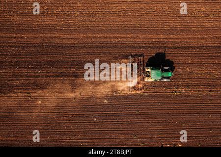 Tracteur avec timon attaché effectuant le travail du sol dans le champ avant la saison de semis, prise de vue aérienne depuis le drone pov haut vers le bas Banque D'Images