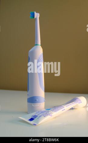 Une photo d'une grande brosse à dents électrique blanche à côté d'un tube de dentifrice pressé. Banque D'Images