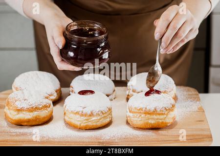 Une femme chef prépare des beignets frais avec de la confiture à sa boulangerie.Cuisine traditionnelle Hanukkah sufganiyot.Concept de petite entreprise. Banque D'Images