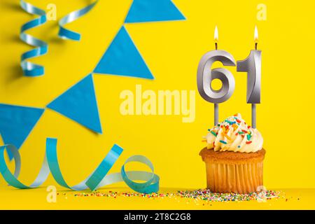 Bougie d'anniversaire numéro 61 avec cupcake - fond jaune avec fanions bleus Banque D'Images