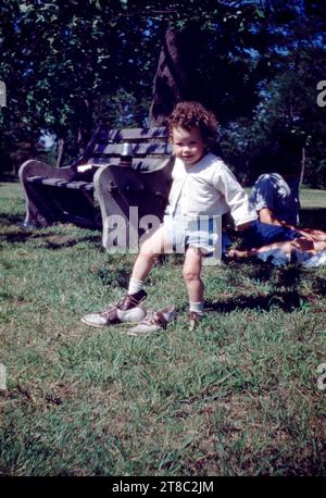 Jeune fille près de Park Bench glissant sur sa chaussure de mère alors que mère repose dans les années 1950 Banque D'Images