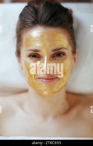 Le temps des soins de santé. Vue supérieure de la femme moderne détendue dans l'armoire de massage avec masque cosmétique doré sur le visage posé sur la table de massage. Banque D'Images