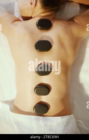 Le temps des soins de santé. Vue supérieure de la femme détendue dans l'armoire de massage ayant massage aux pierres chaudes et s'étendant sur la table de massage. Banque D'Images