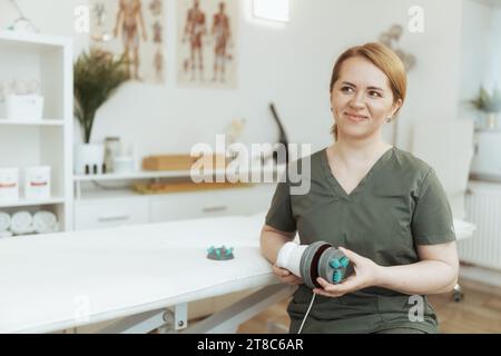 Le temps des soins de santé. thérapeute de massage médical féminin souriant dans l'armoire de massage avec des accessoires de massage. Banque D'Images