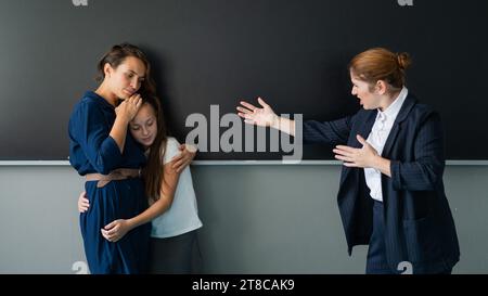 L'enseignante crie à la jeune fille et à sa mère debout au tableau noir. Banque D'Images