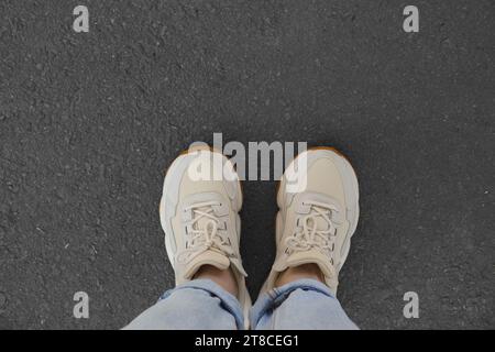 Femme en baskets blanches debout sur l'asphalte, vue de dessus Banque D'Images