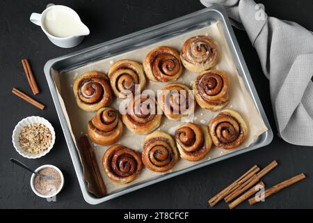 Petits pains à la cannelle savoureux dans un plat allant au four sur une table en bois noir, plat Banque D'Images