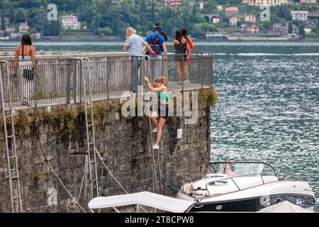 Une femme grimpe sur une échelle d'une jetée à son hors-bord mal amarré ci-dessous à la Punta Spartivento sur le lac de Côme à Bellagio, Lombardie, Italie. Banque D'Images