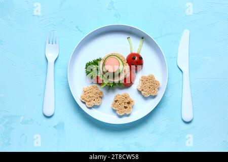 Assiette avec petit déjeuner drôle pour enfants en forme d'escargot sur la table bleue Banque D'Images