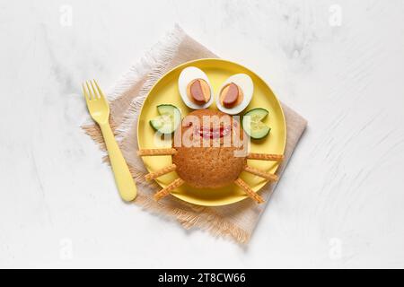 Assiette avec le petit déjeuner drôle des enfants en forme de crabe sur la table blanche Banque D'Images