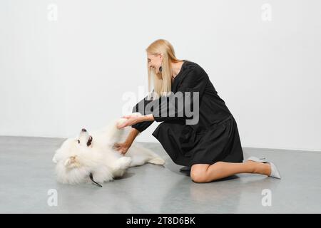 Joyeuse femme blonde jouant avec un chien samoyed tenant sa patte Banque D'Images