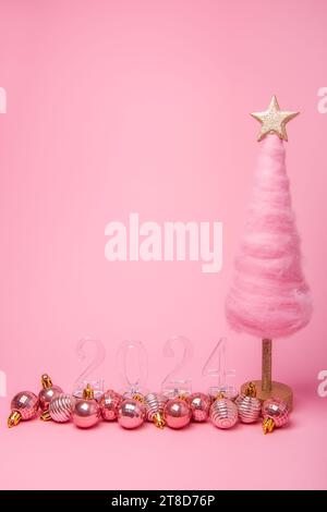 Arbre de Noël créatif pelucheux de fond rose vif isolé en laine, numéros transparents 2024 avec des boules brillantes. Carte de vacances du nouvel an. Templat Banque D'Images