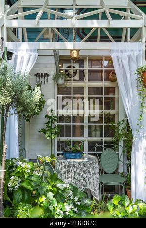 patio avec chaises et tables à l'ombre parmi les plantes et les fleurs près de la fenêtre Banque D'Images