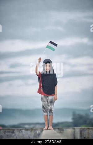 Mignonne petite fille agitant le drapeau de Palestine envoie un message puissant de soutien et d'empathie au monde Banque D'Images