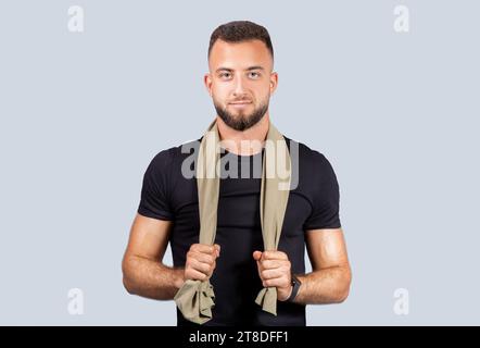 Positif confiant fort jeune homme caucasien entraîneur en vêtements de sport noirs, avec serviette, regardez la caméra Banque D'Images