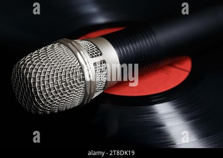 Le microphone repose sur un disque vinyle, avec la réflexion de la lumière soulignant les pistes sonores. Concept d'enregistrement sonore analogique Banque D'Images