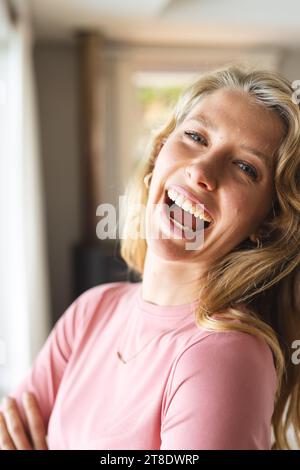 Femme caucasienne blonde heureuse debout et riant dans le salon ensoleillé à la maison Banque D'Images