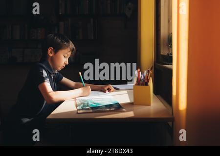 Garçon dessine à la table dans sa chambre par une journée ensoleillée Banque D'Images