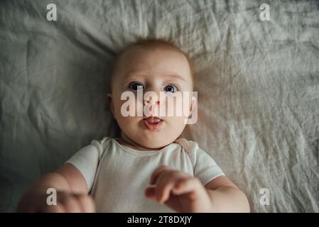 Gros plan au-dessus de la tête de bébé allongé sur le lit et sortant de la langue Banque D'Images