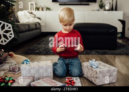 Petit garçon regarde vers le bas à envelopper ruban tout en étant assis dans la vie Banque D'Images