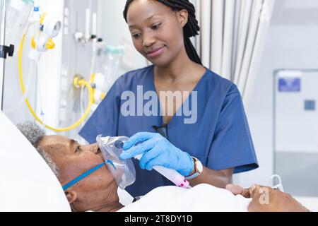 Médecin afro-américaine appliquant un masque à oxygène à une patiente âgée en chambre d'hôpital Banque D'Images