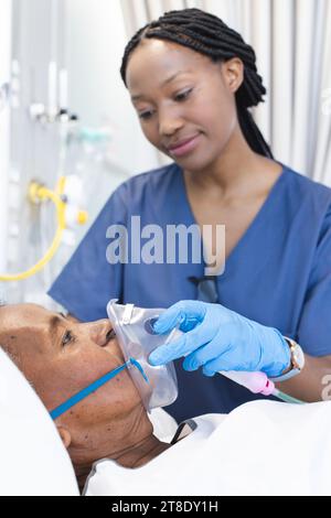 Médecin afro-américaine appliquant un masque à oxygène à une patiente âgée en chambre d'hôpital Banque D'Images