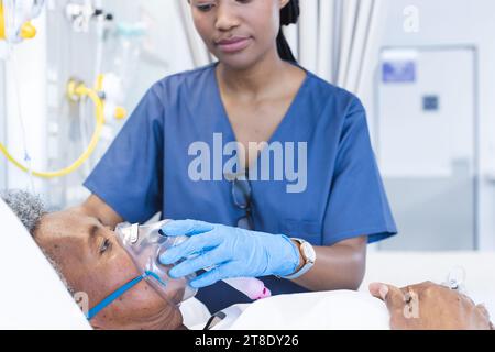 Médecin afro-américaine appliquant un masque à oxygène à une patiente âgée en chambre d'hôpital Banque D'Images