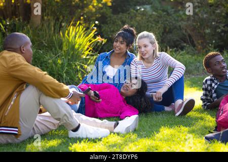 Heureux et divers amis adolescents parlant et assis sur l'herbe dans le parc Banque D'Images
