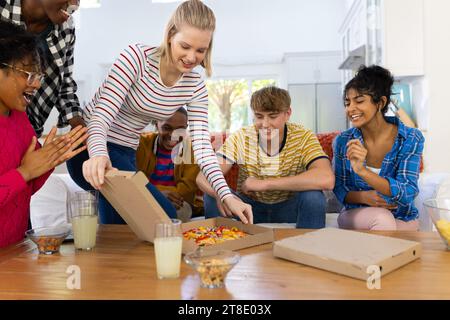 Heureux groupe diversifié d'amis adolescents assis sur le canapé et mangeant de la pizza Banque D'Images