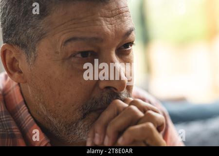 Homme biracial senior réfléchi portant une chemise à carreaux et se tenant les mains à la maison Banque D'Images