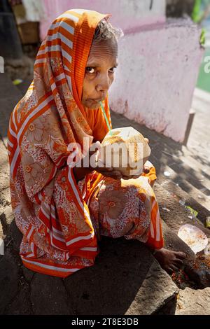 Une vieille veuve hindoue vêtue de sari assise près du Banganga Tank sacré à Walkeshwar, Mumbai, Inde, se rafraîchissant avec de l'eau de coco fraîche Banque D'Images