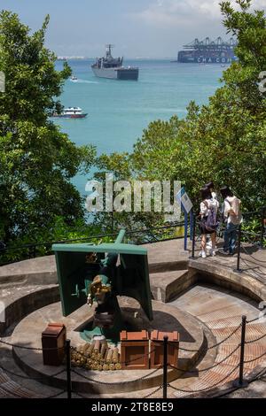 Vue verticale des touristes vérifient l'explication du signe, un navire de la marine en arrière-plan. Fort Siloso, Sentosa, Singapour. Banque D'Images