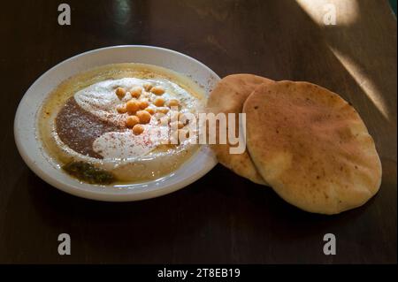 Houmous frais sur une assiette avec pois chiches de haricots entiers, sauce aux haricots et tahini, servi avec deux morceaux de pain pita rond entier. Banque D'Images